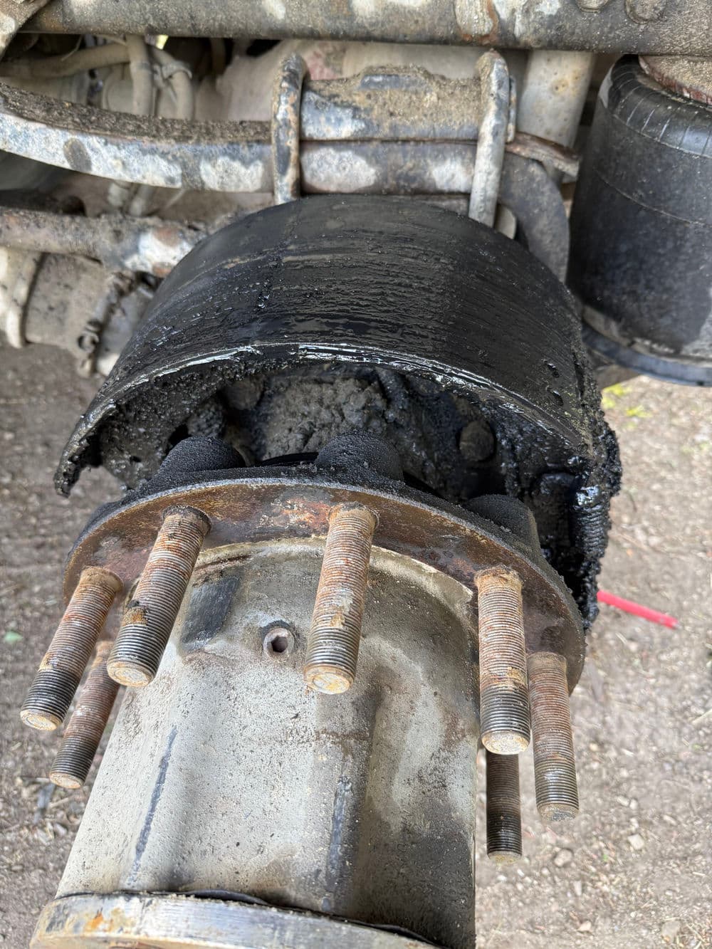 Damaged brake drum with excessive grease buildup on vehicle axle assembly.