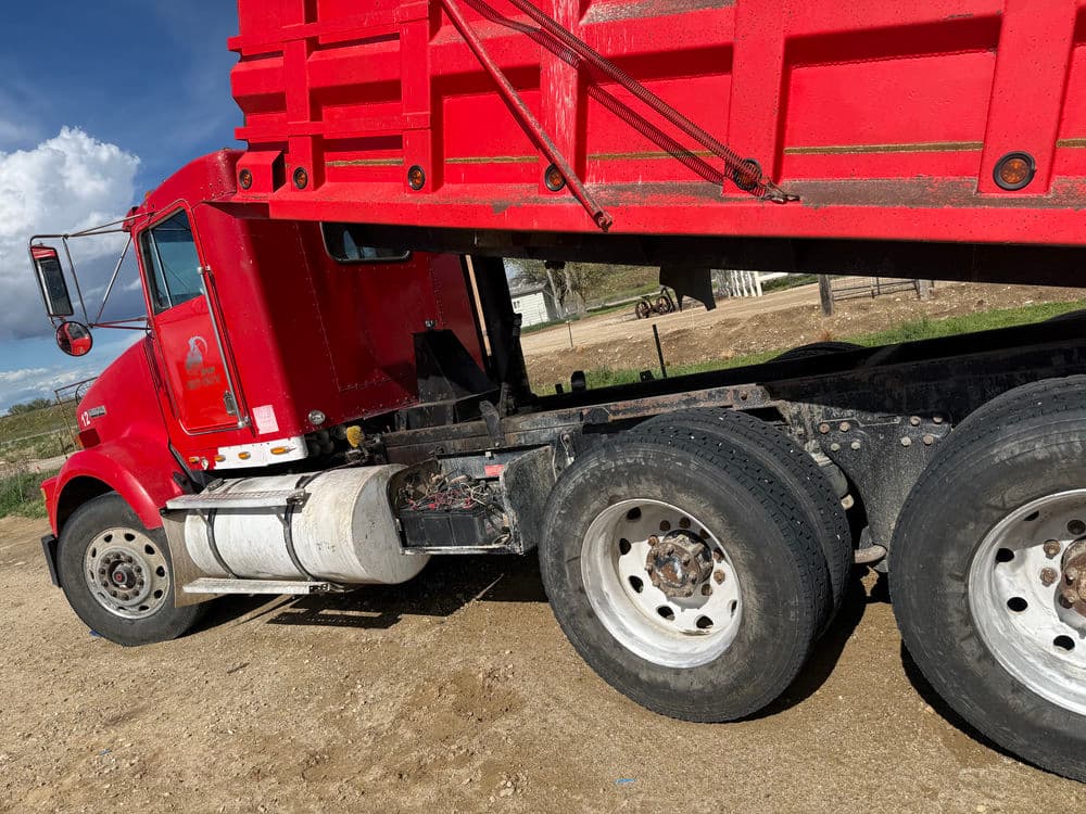 Red dump truck parked on a dirt road, showcasing its tires and side profile.