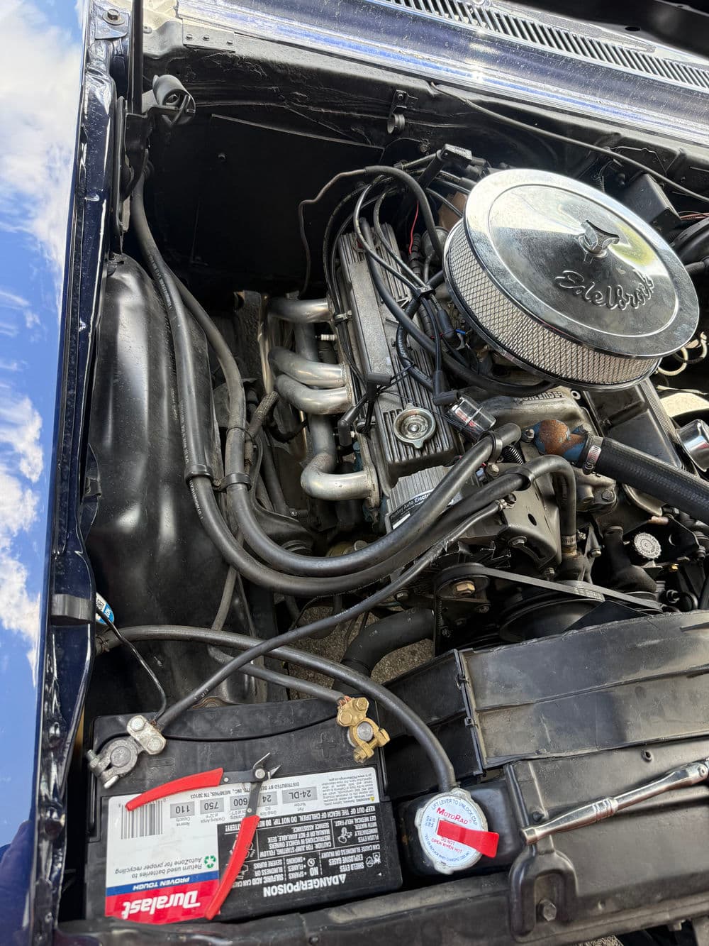 Engine compartment view showing a performance carburetor and battery in a classic car.