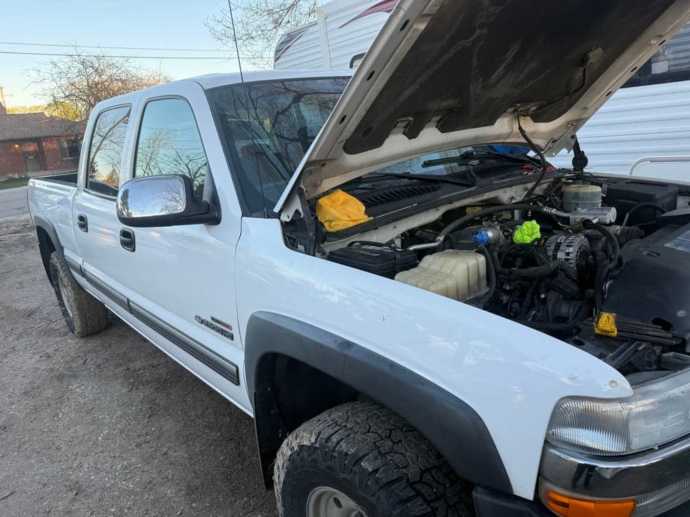 White pickup truck with hood open, showing engine and maintenance in a driveway setting.