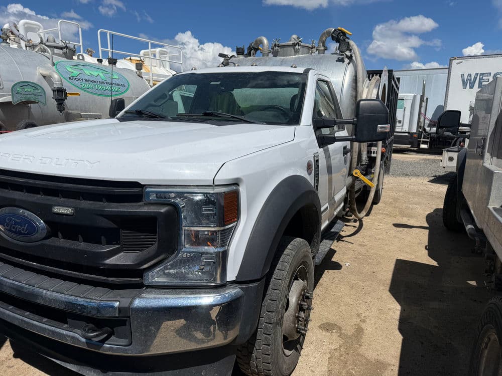 White Ford Super Duty truck parked among various service vehicles on a sunny day.