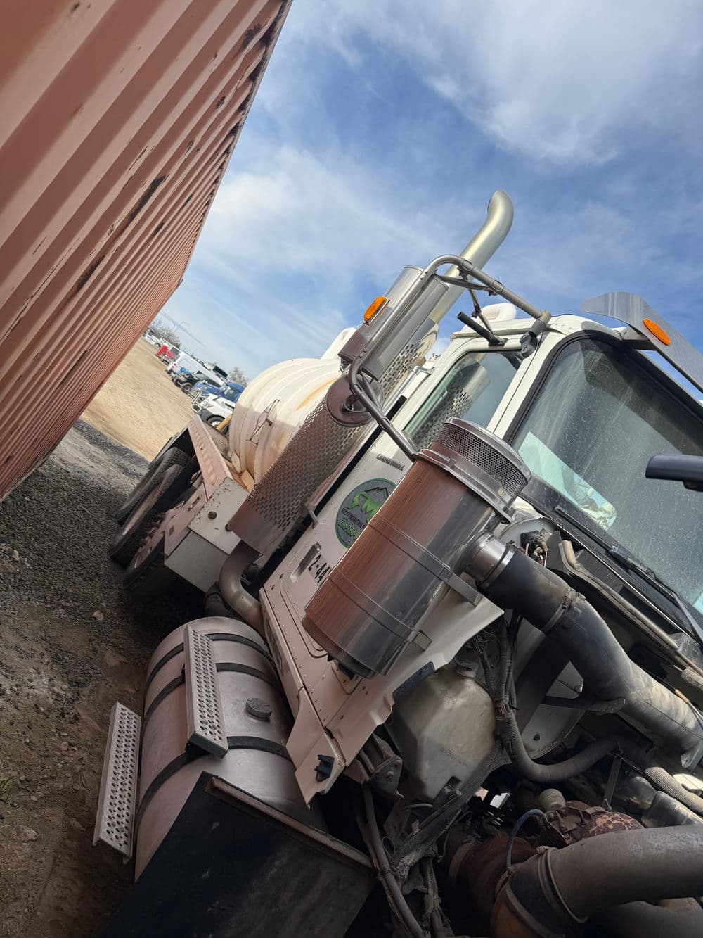 Side view of a white industrial truck parked next to a shipping container on a gravel lot.