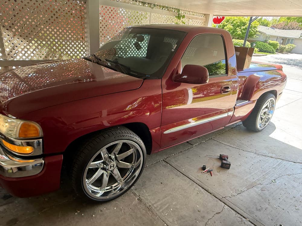 Red pickup truck with chrome wheels parked under a carport, tools nearby.
