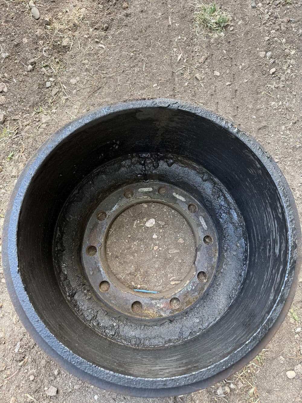 Rusty metal wheel rim viewed from above, showing dirt and debris inside the hollow center.