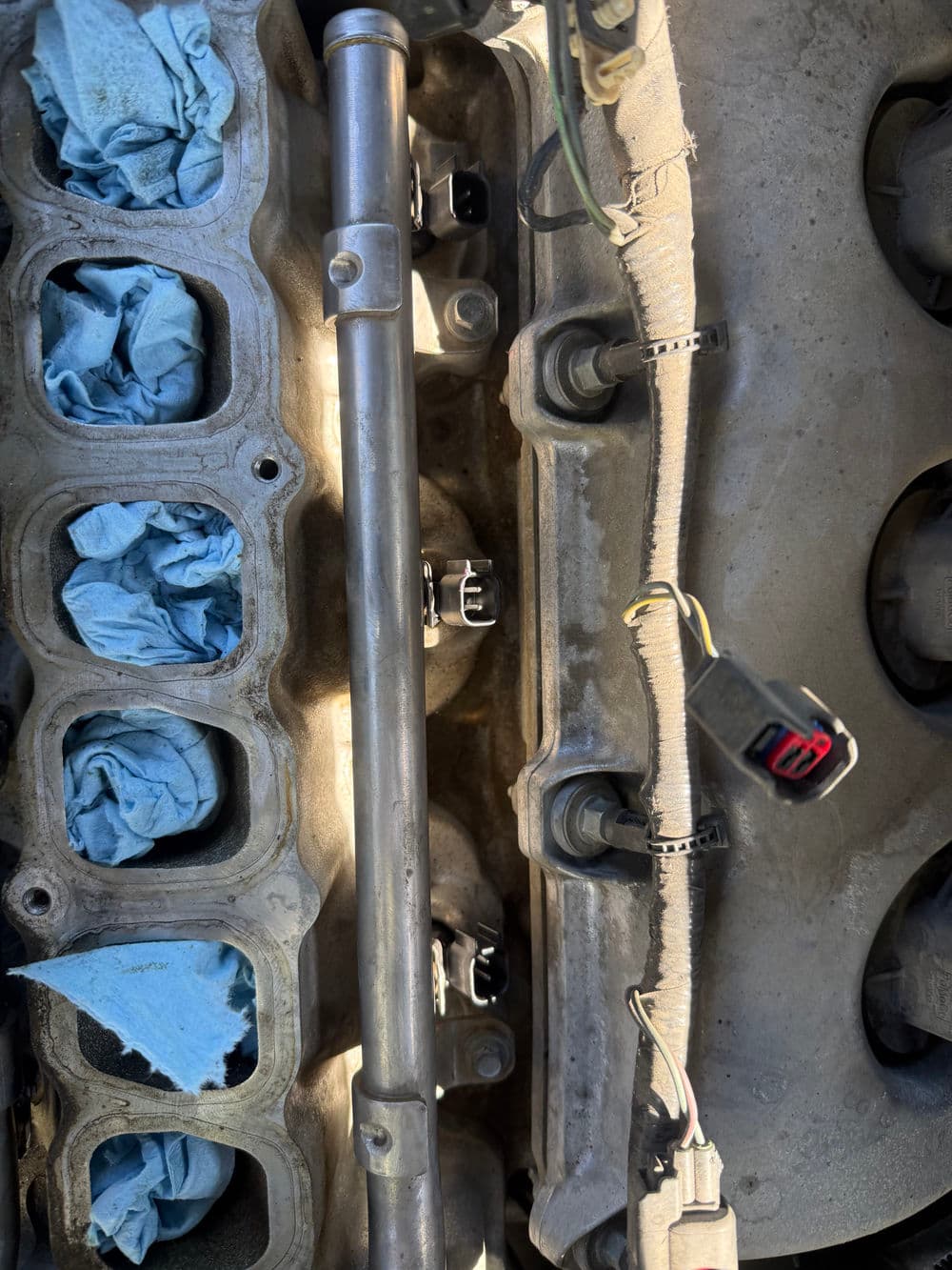Close-up of an engine manifold with blue rags and fuel injector connectors.