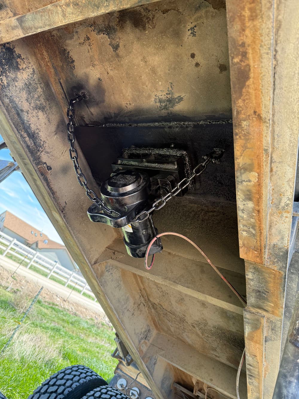 Detail of a trailer hitch mechanism with chain and electrical connections, showing wear and rust.