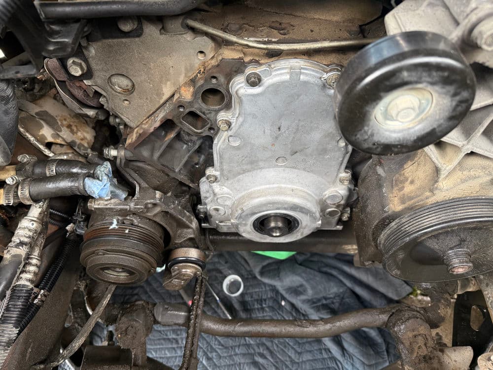 Close-up of an engine assembly showing the timing cover and pulleys in a vehicle.