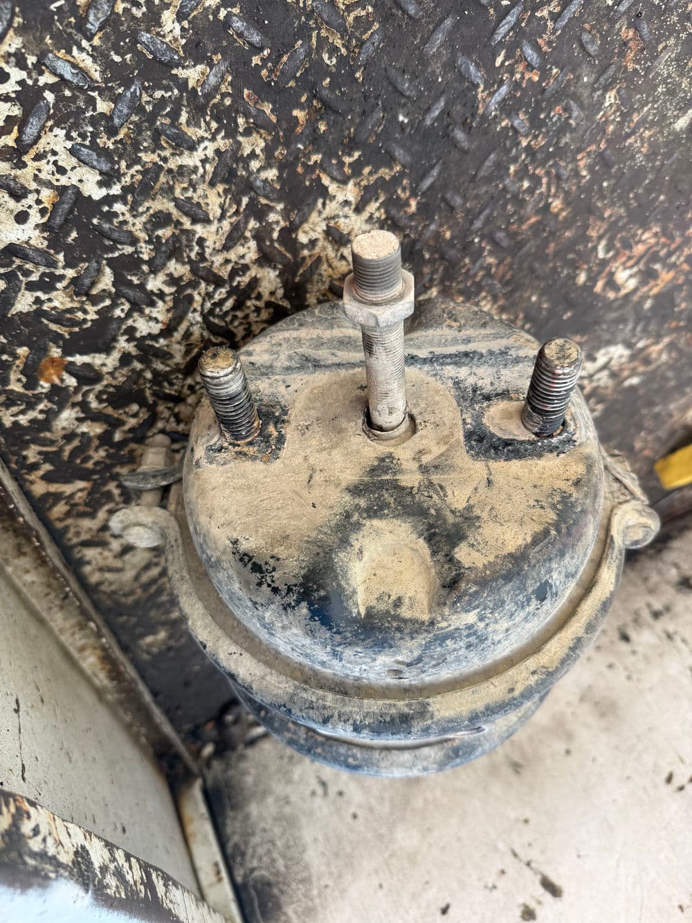 Dirty automotive air suspension component with three mounting bolts.