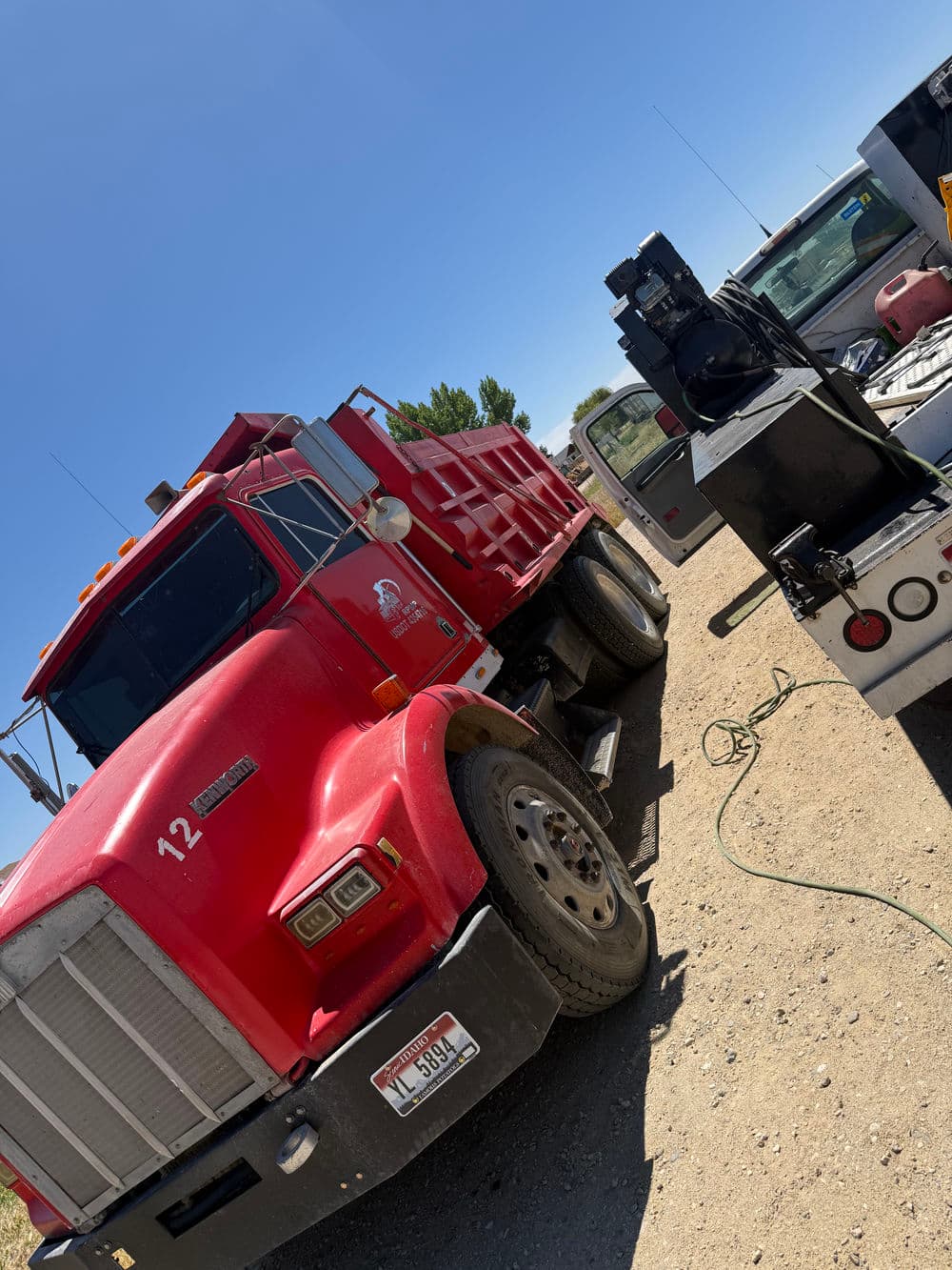 Red dump truck parked in a construction area with equipment and vehicles in the background.