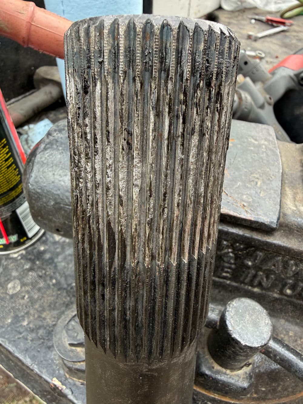 Worn vehicle drive shaft with visible grooves and dirt on a workshop bench.