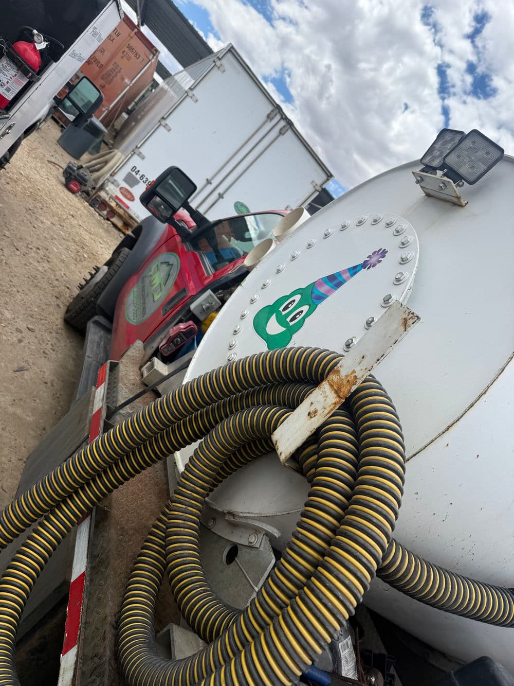 Red truck with whimsical green character sticker and yellow hose on industrial site.