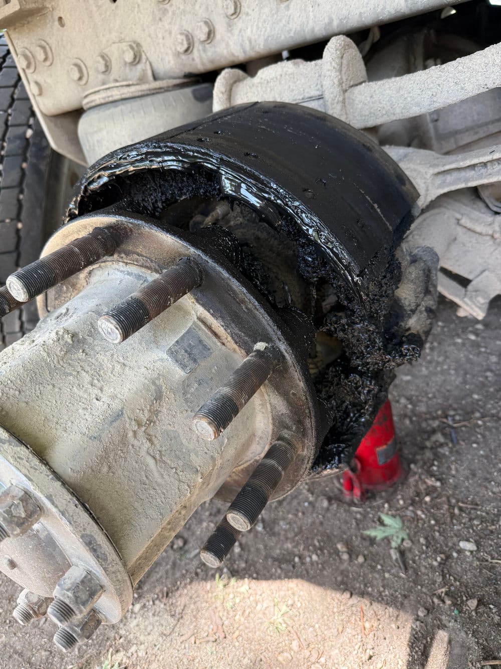 Damaged truck wheel hub with black grease and dirt buildup, showing wear and tear.