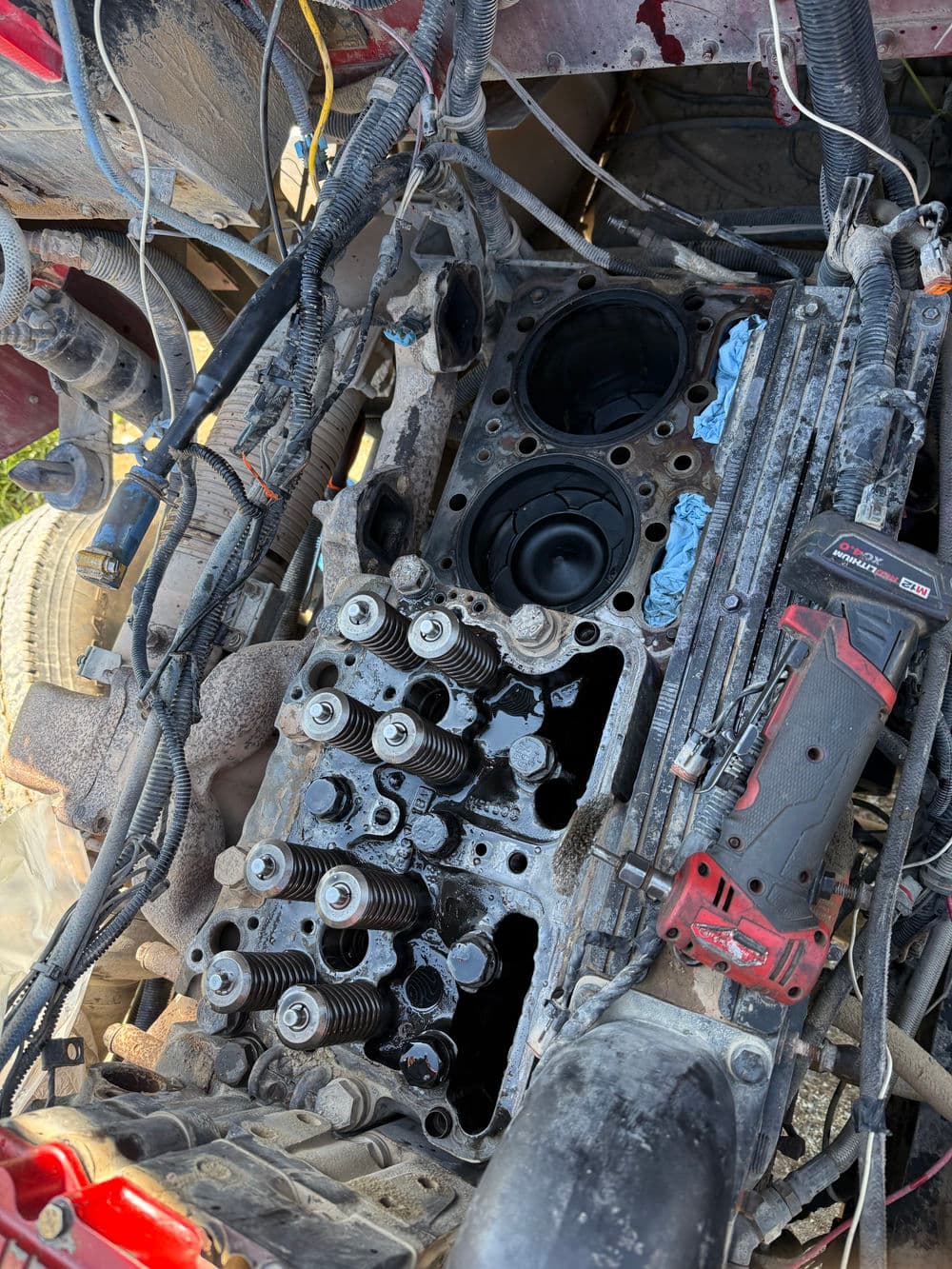 Disassembled engine showing cylinder head, valves, and tools on a dirty work surface.