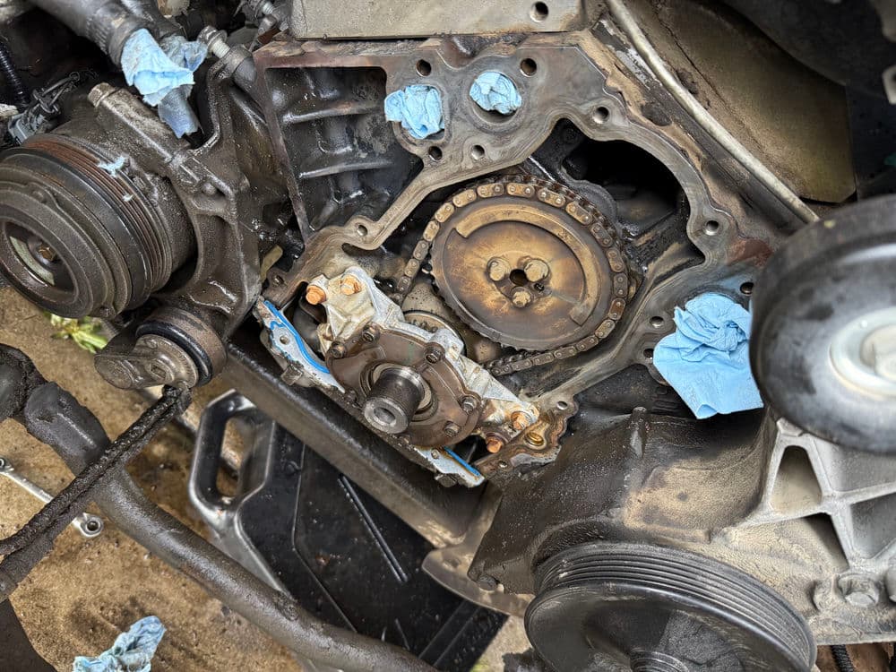 Engine components with timing chain, repair tools, and blue shop towels on a garage floor.