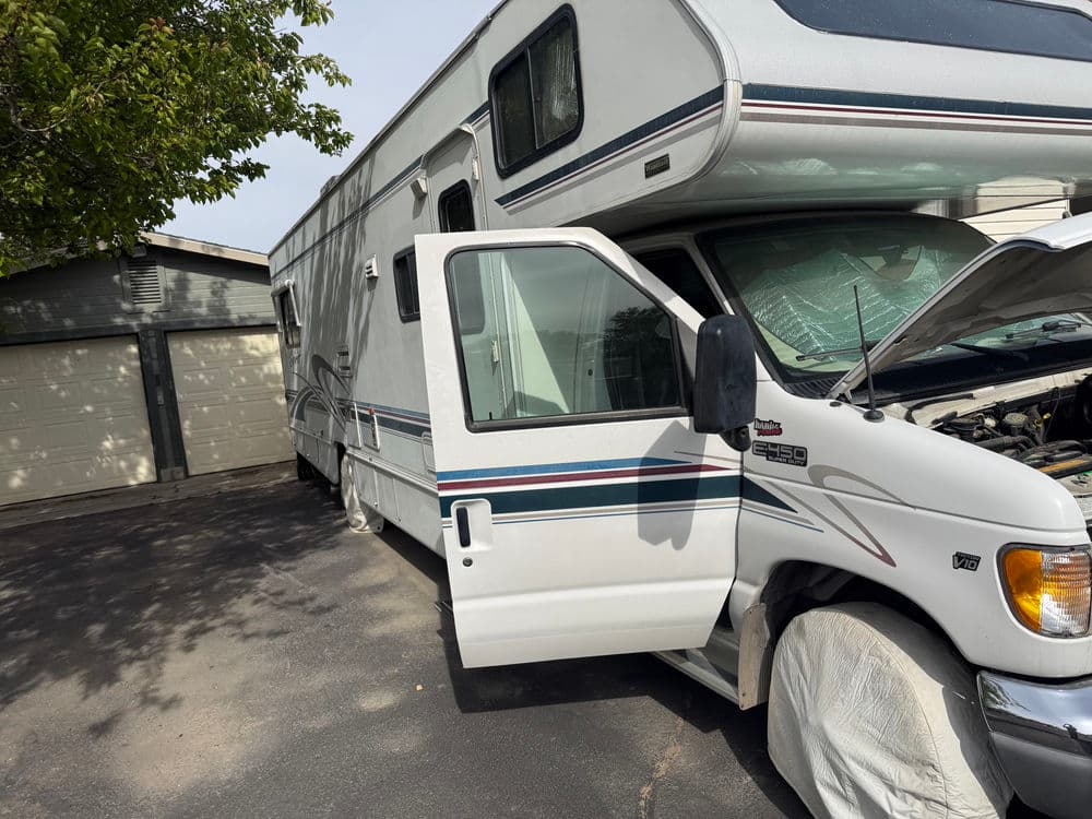 White RV parked with its door open, showing a partially visible engine in a driveway.