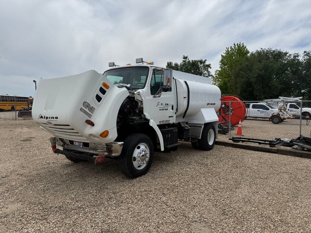 Alpine vacuum truck parked in a gravel area with equipment in the background.