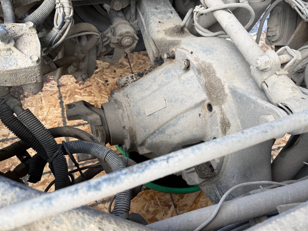 Close-up of a dirty vehicle transfer case and surrounding components in an auto repair setting.