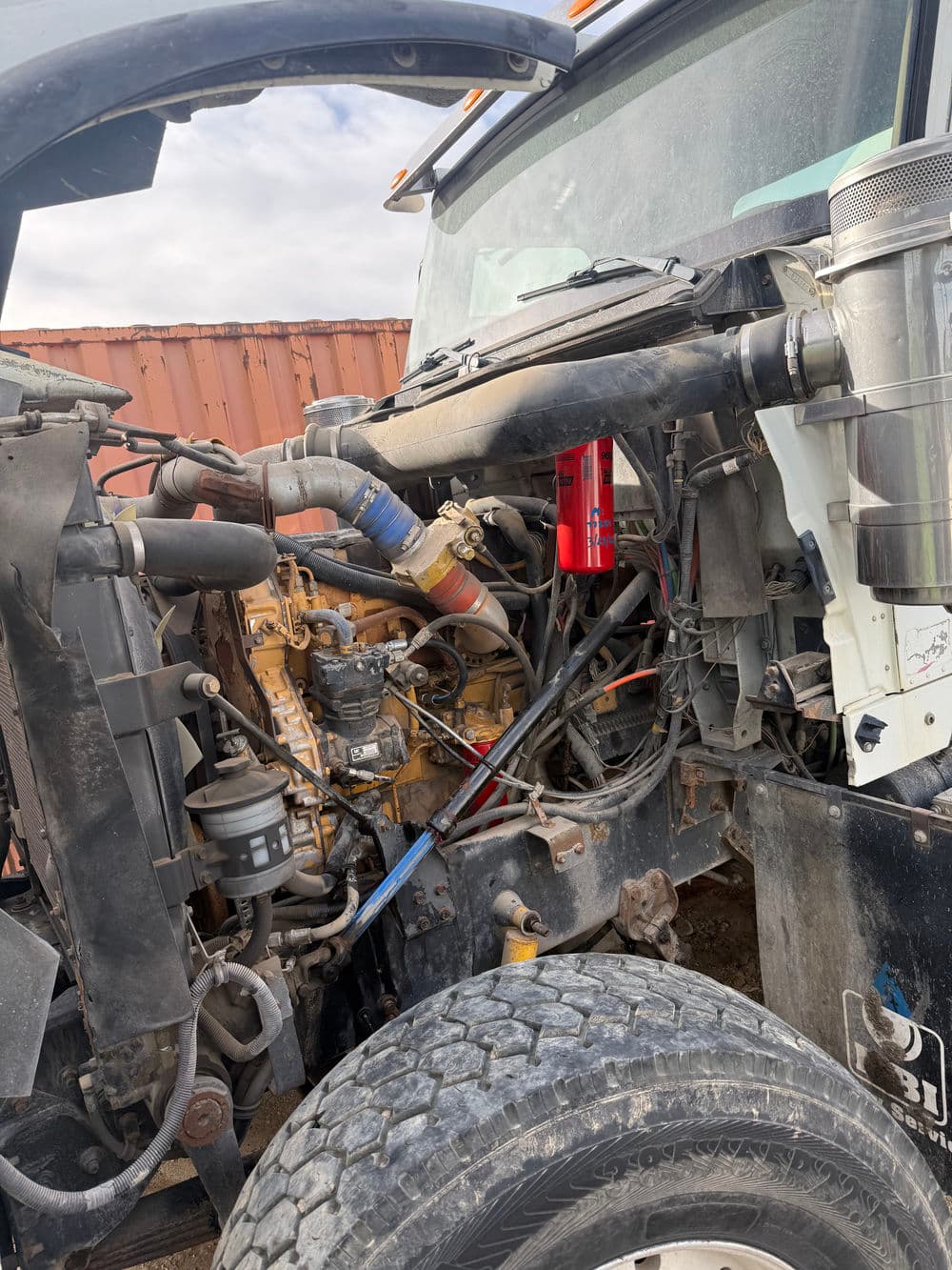 Close-up of a truck engine compartment showing pipes, hoses, and mechanical components.