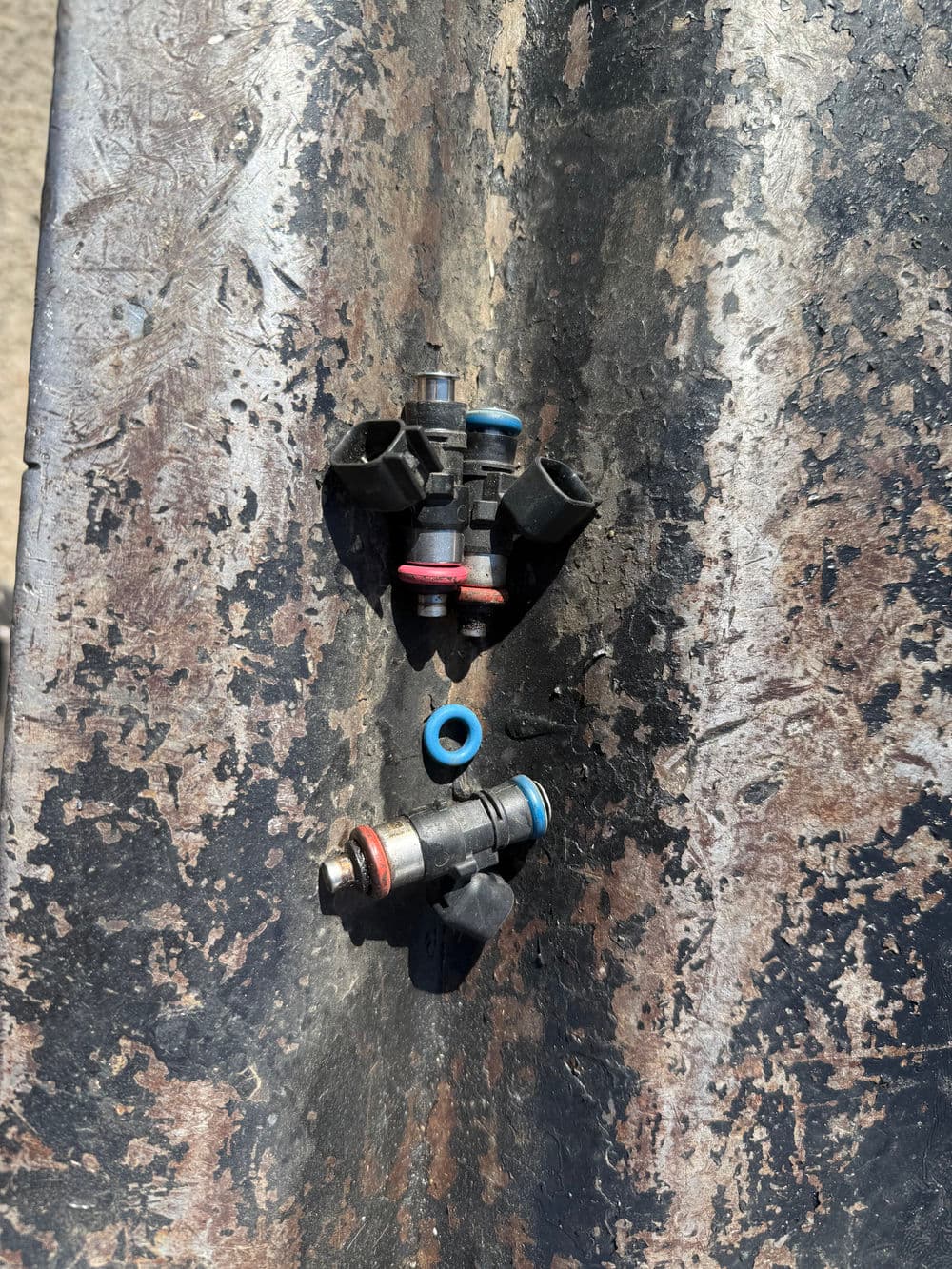 Two automotive fuel injectors displayed on a textured metal surface.