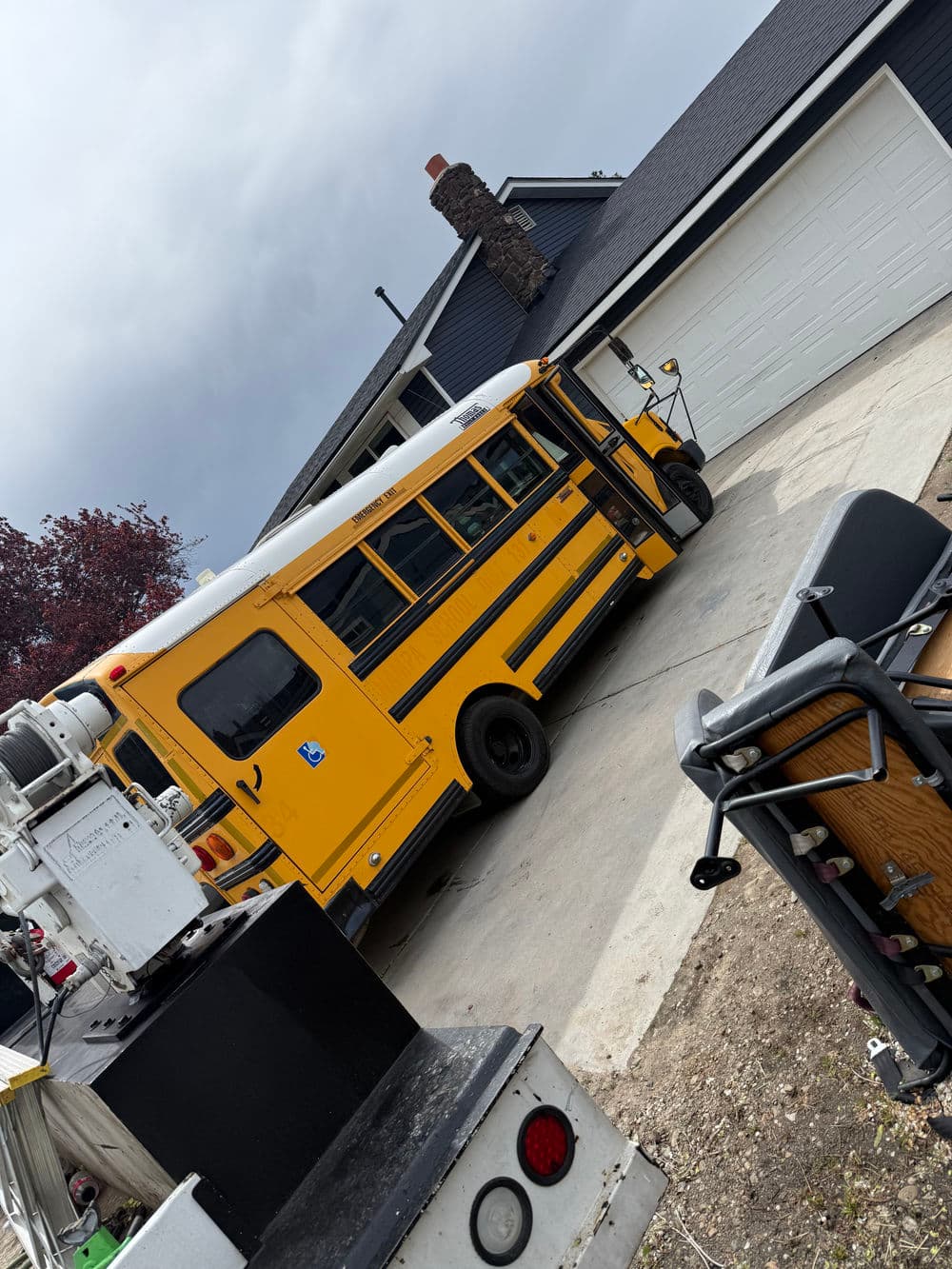 Yellow school bus parked in a driveway near a garage and outdoor equipment.