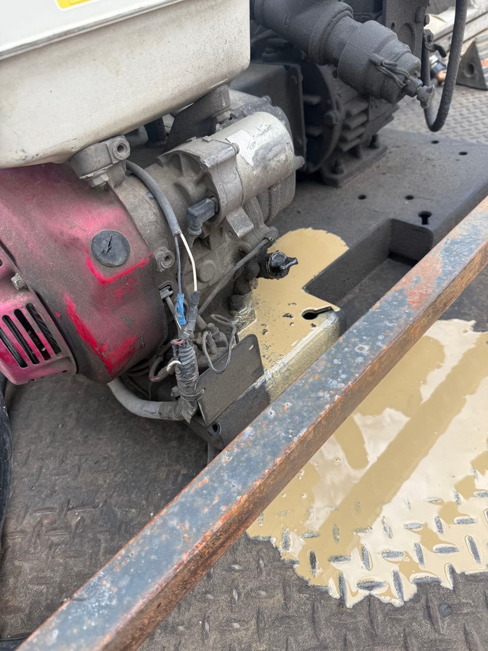 Close-up of an engine with visible wiring and oil spill on a metal surface.