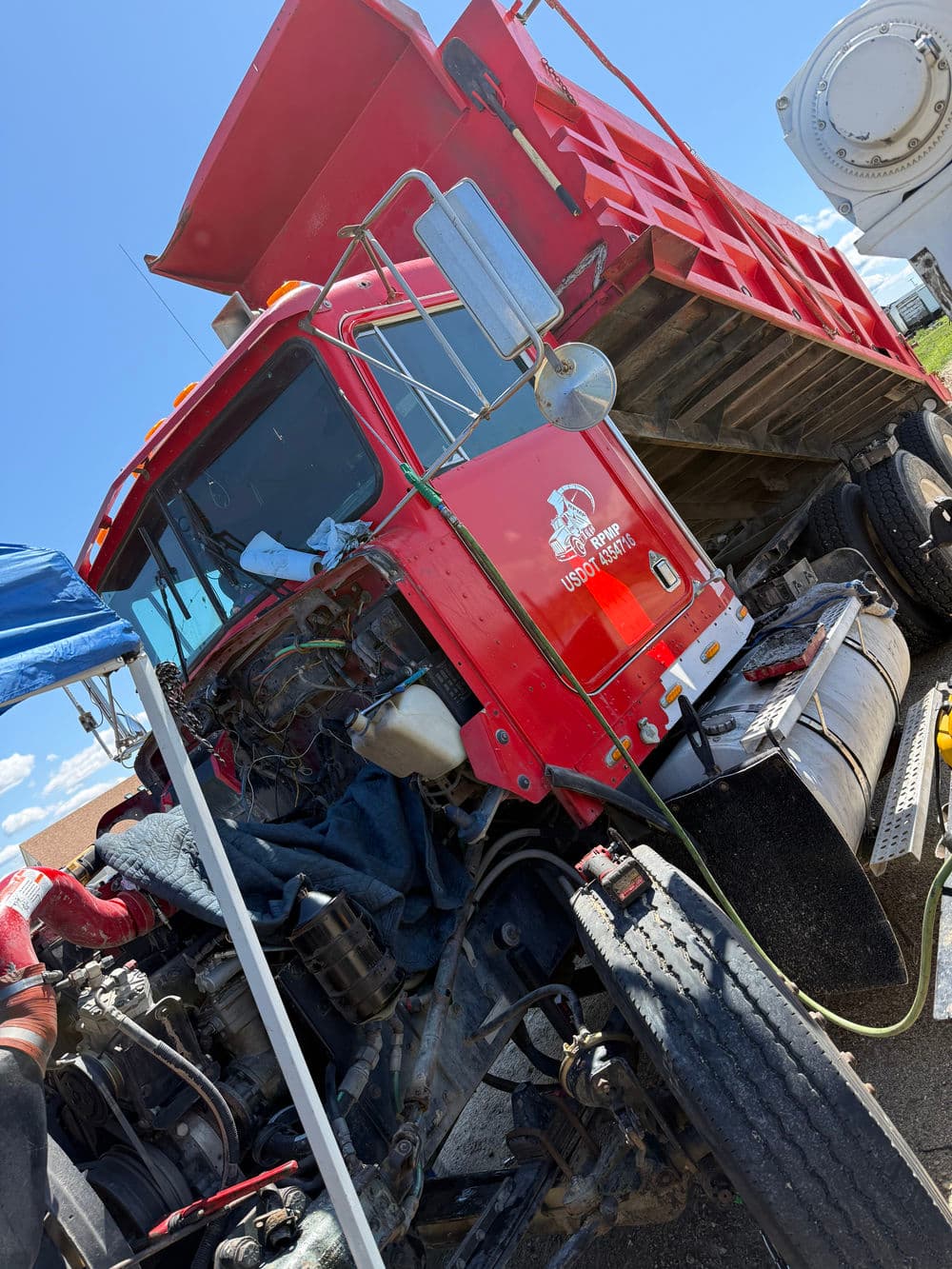 Red dump truck with visible engine components and wear on the tires, parked outdoors.