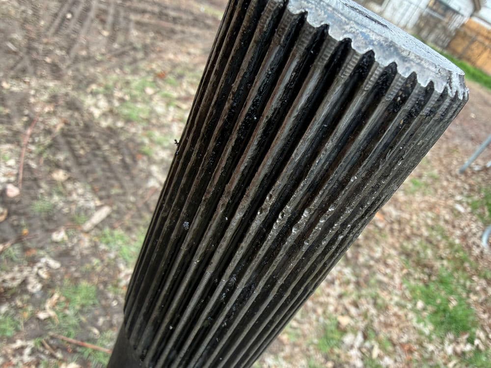 Close-up of a textured black post with vertical grooves in a grassy outdoor setting.