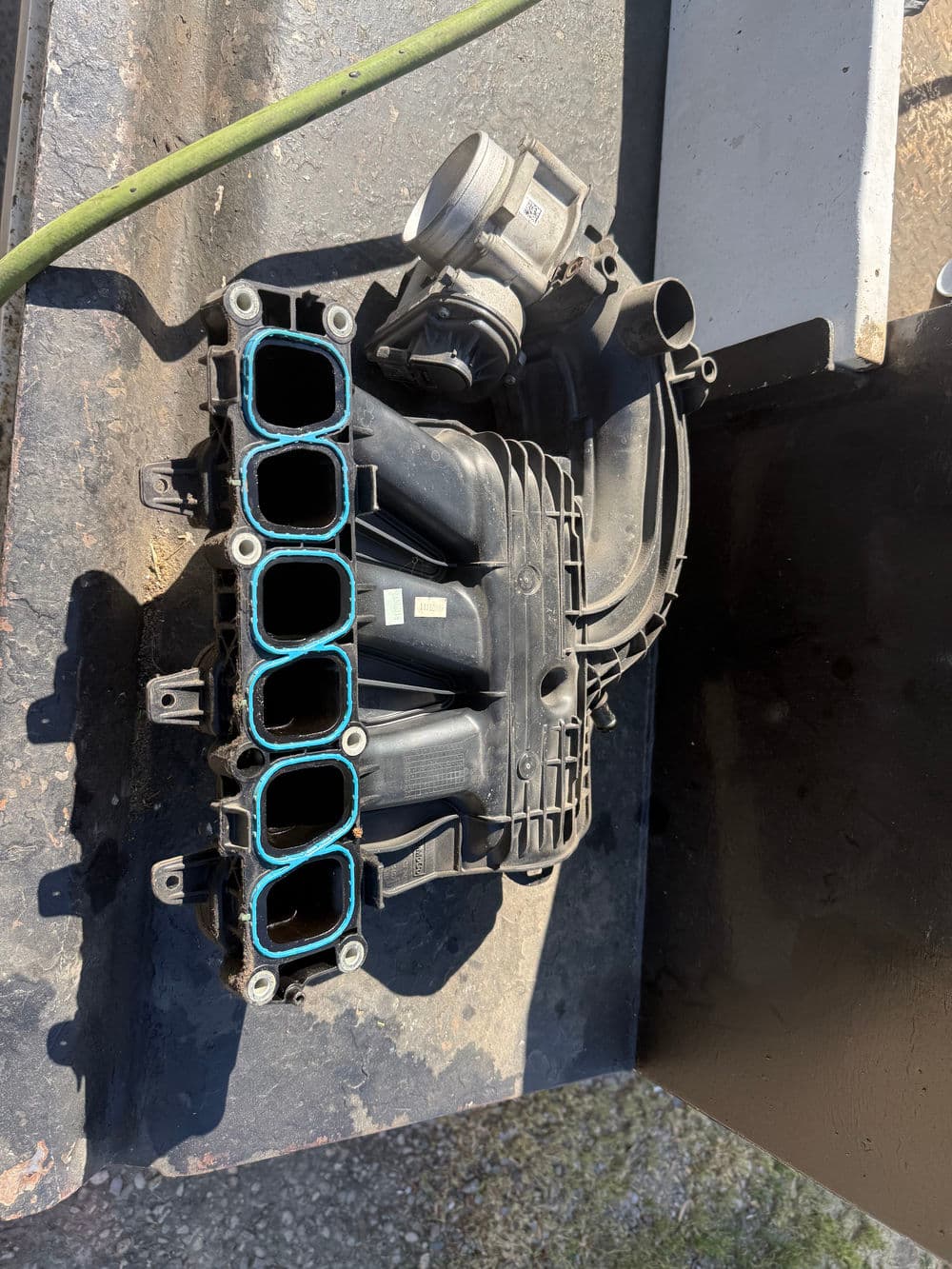 Automotive intake manifold on a workbench for engine repairs and modifications.